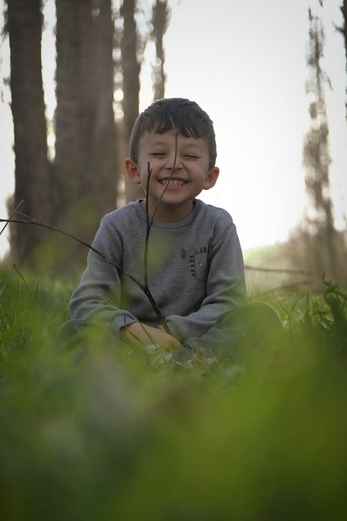 Free A young boy sitting in the grass with a stick Stock Photo