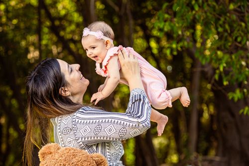 Free A joyful mother lifting her smiling baby in a sunlit forest, capturing a moment of happiness. Stock Photo