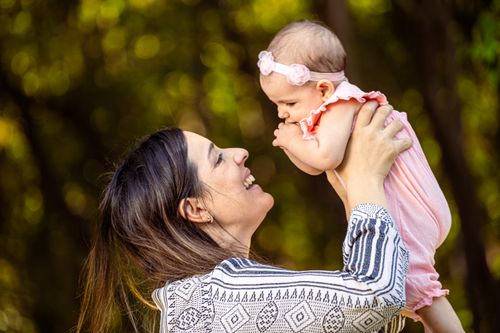 Free Joyful mother lifting her smiling baby outside on a sunny day, showcasing love and connection. Stock Photo