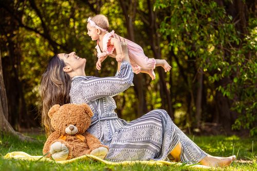 Free Woman plays with baby in forest setting, with teddy bear beside them. Stock Photo