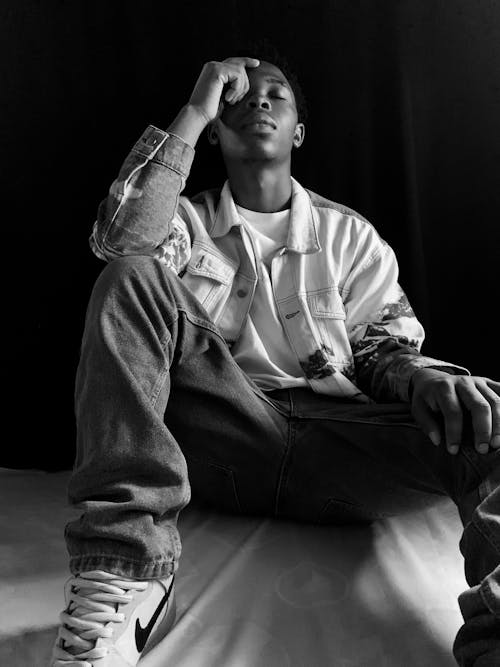 A young man sitting on a bed with his hands on his head