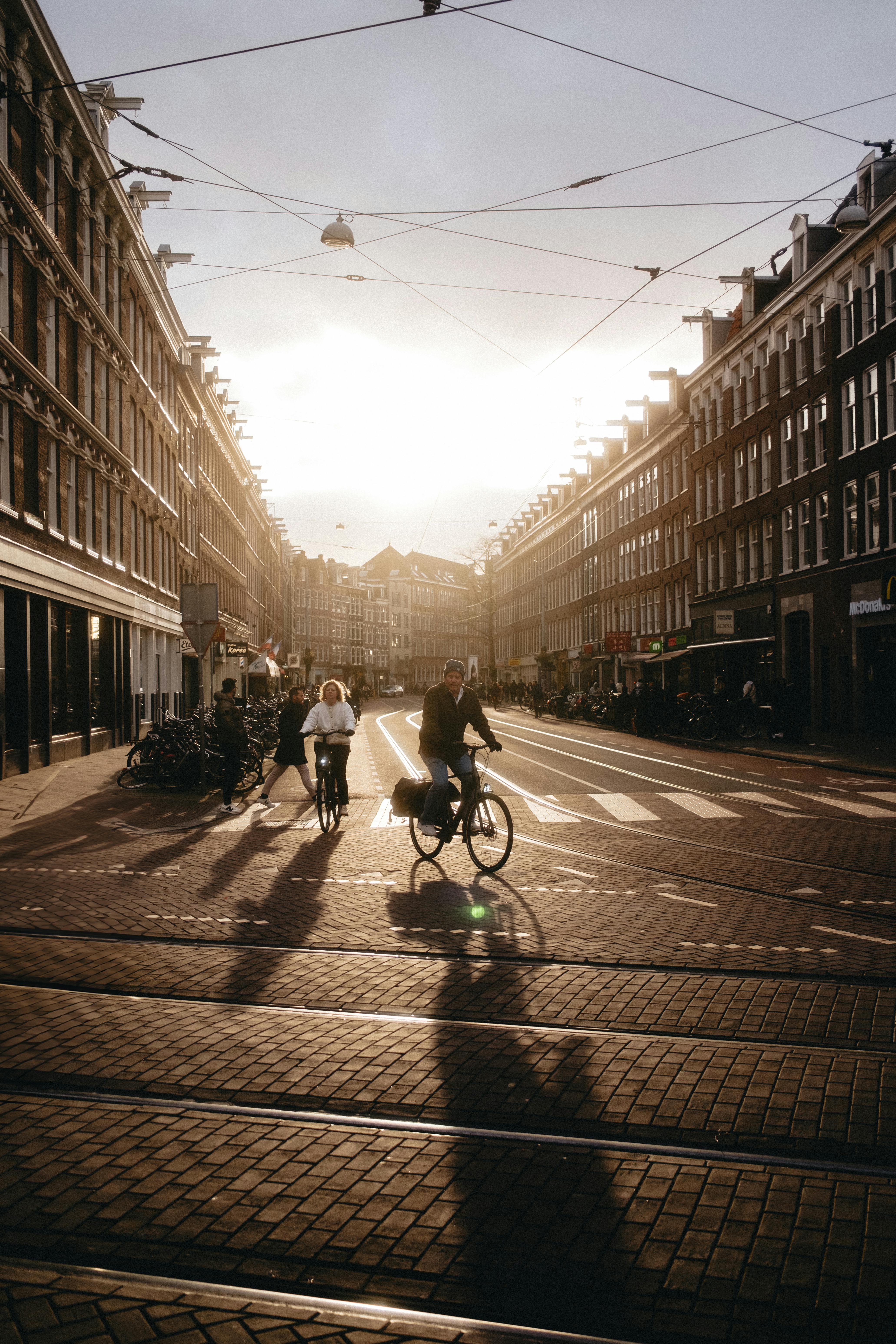 Cyclists ride through a sunlit street in Amsterdam, capturing the vibrant urban life at sunset.