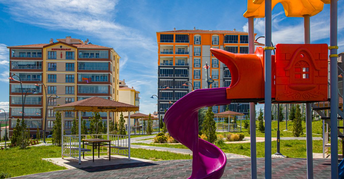 Vibrant playground with a slide in a green urban park amidst modern buildings.