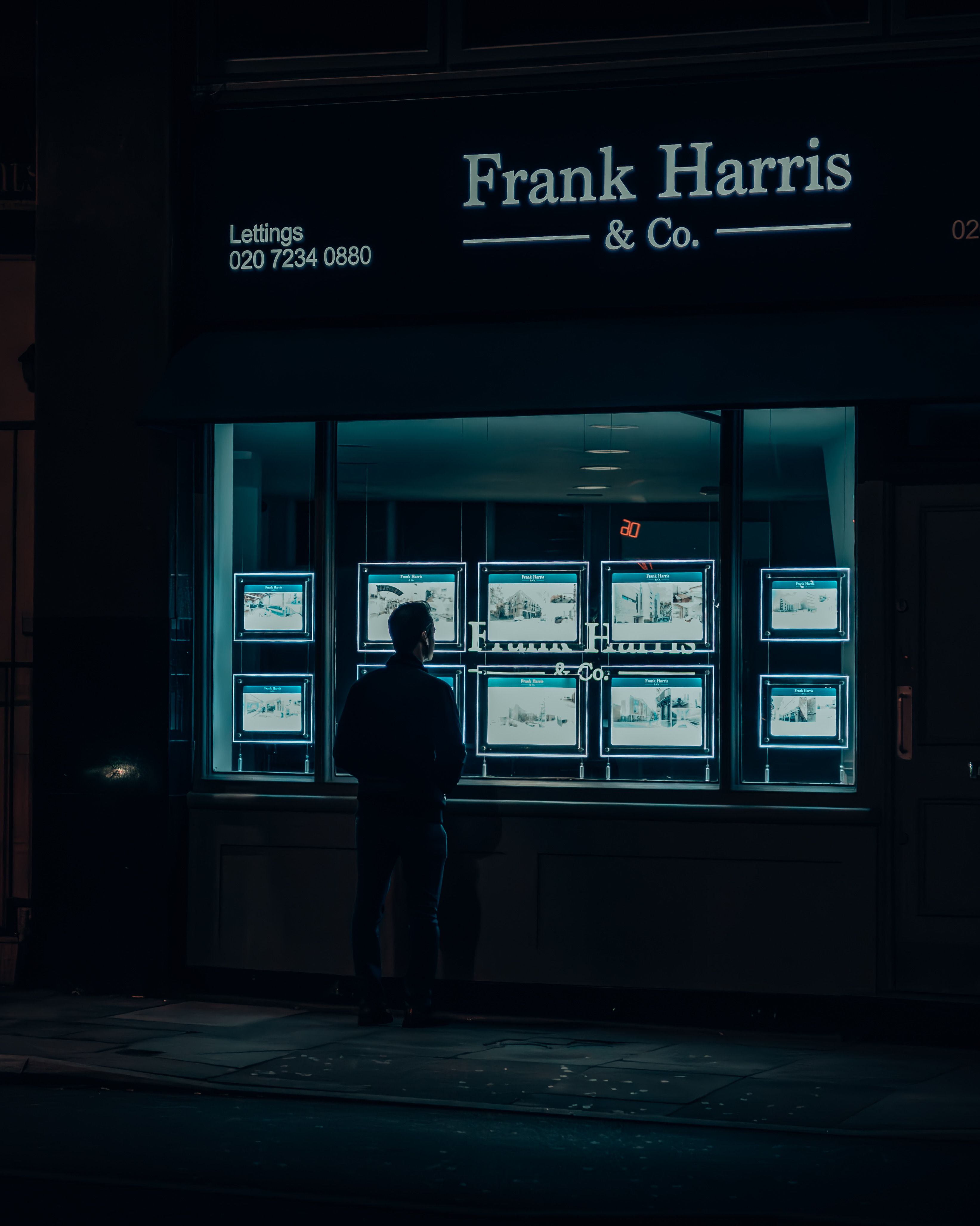 Silhouette of a man viewing illuminated real estate listings at night in a city.