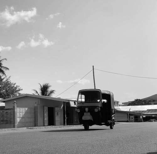 A black and white photo of a tuk tuk driving down the street