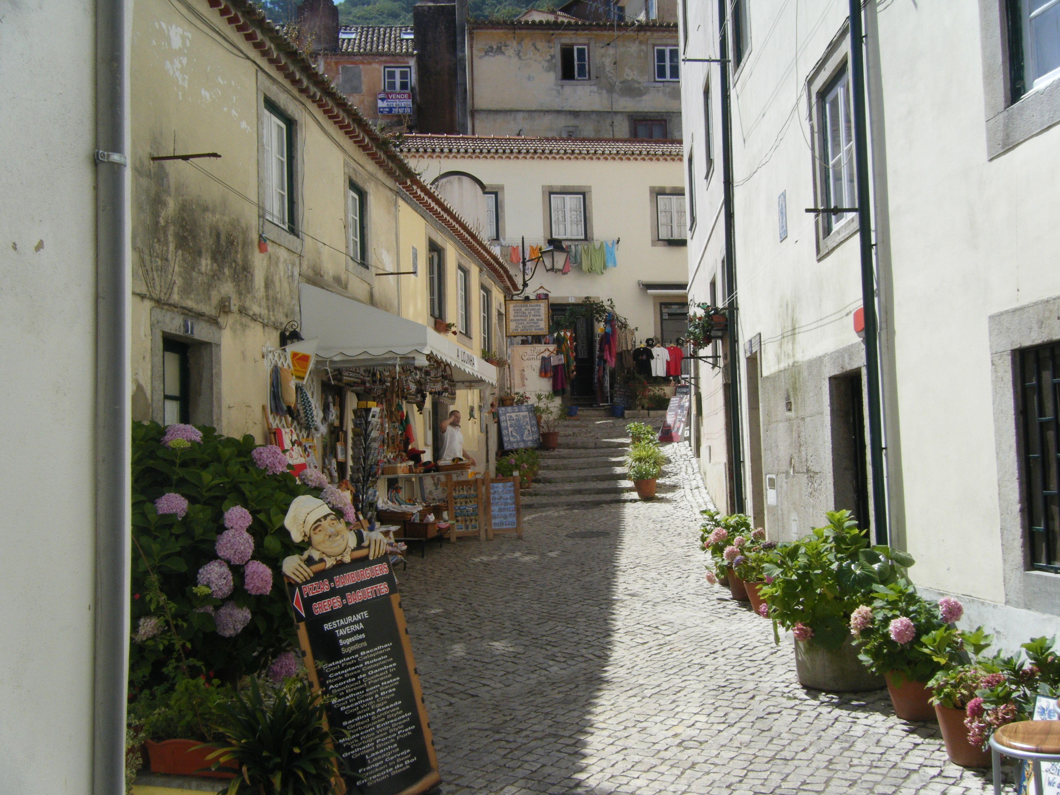 Steep Mouraria lane with a fado mural, hanging laundry and small immigrant-run shops