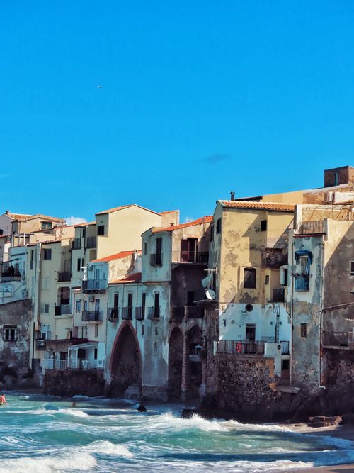 Free Rustic buildings line the coast in colorful Cefalù, Sicily under a clear blue sky. Stock Photo