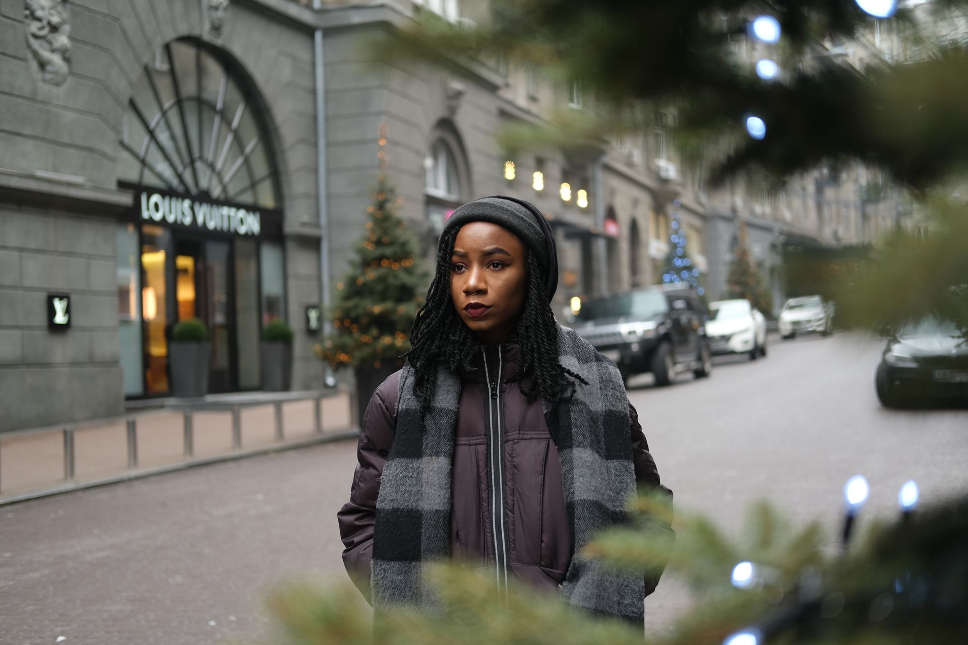 A fashionable woman in winter attire standing on a city street, near a luxury store.