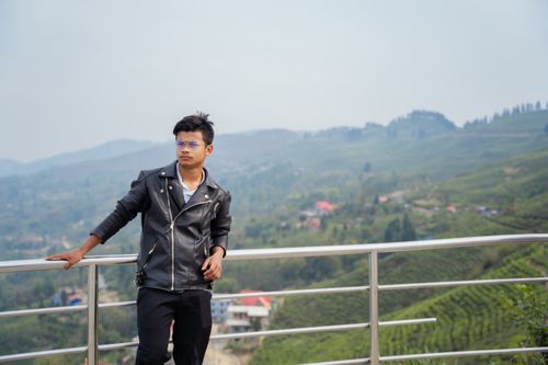 Free A young man in a leather jacket poses against a scenic mountain view, conveying leisure and style. Stock Photo