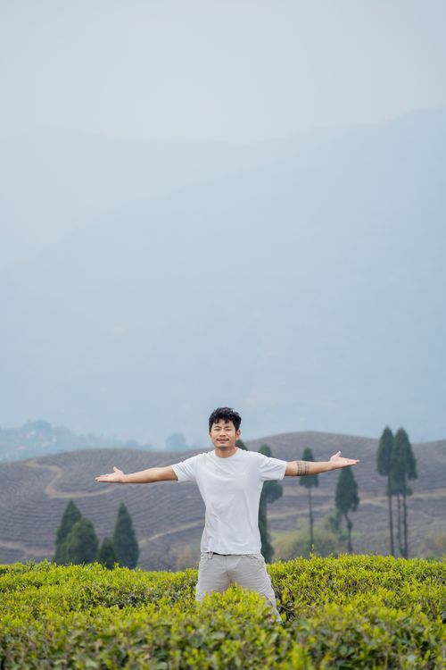 Free Asian man with open arms standing amidst lush tea plantation, expressing freedom and leisure. Stock Photo