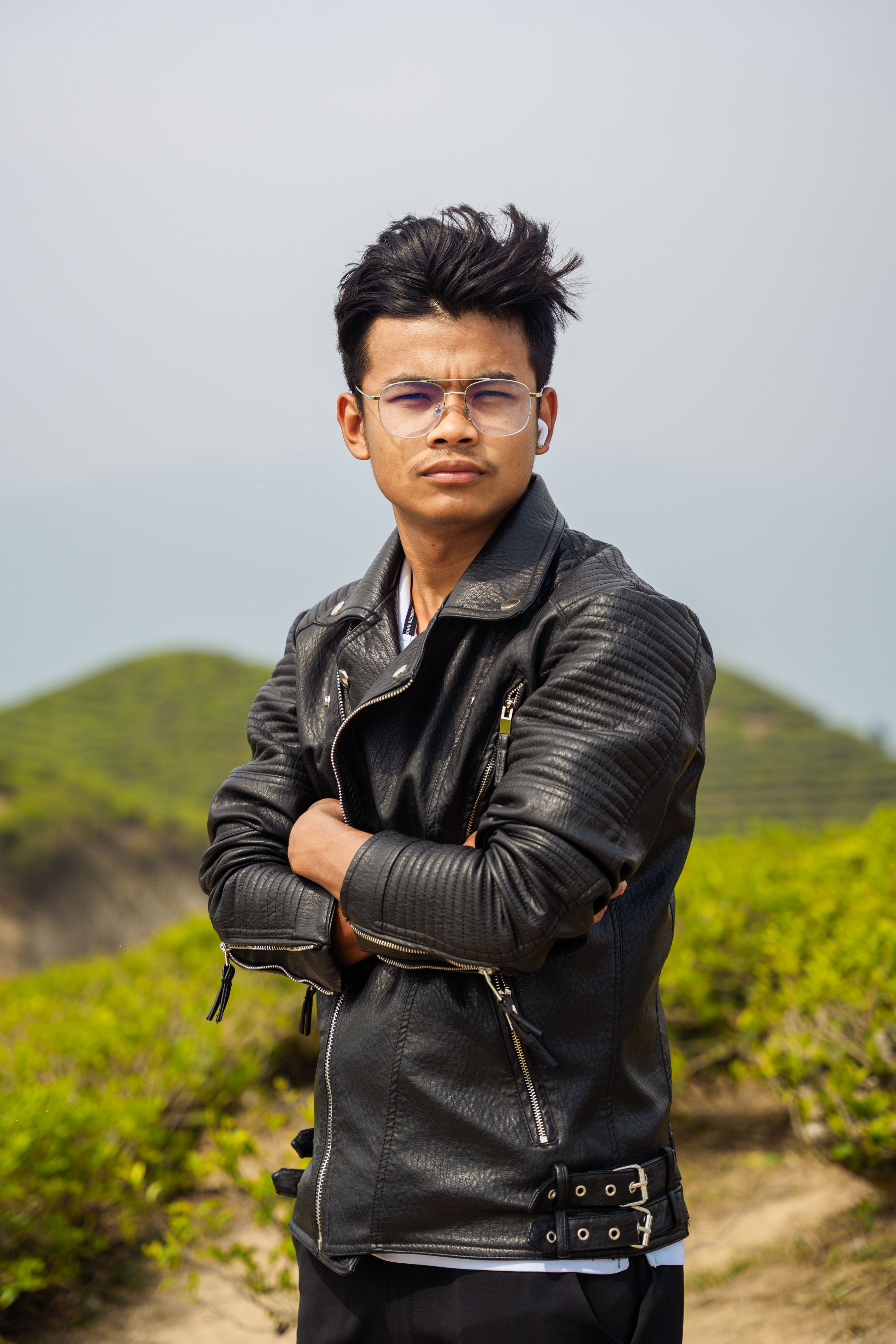 Confident young man in leather jacket posing outdoors at a scenic tea plantation.