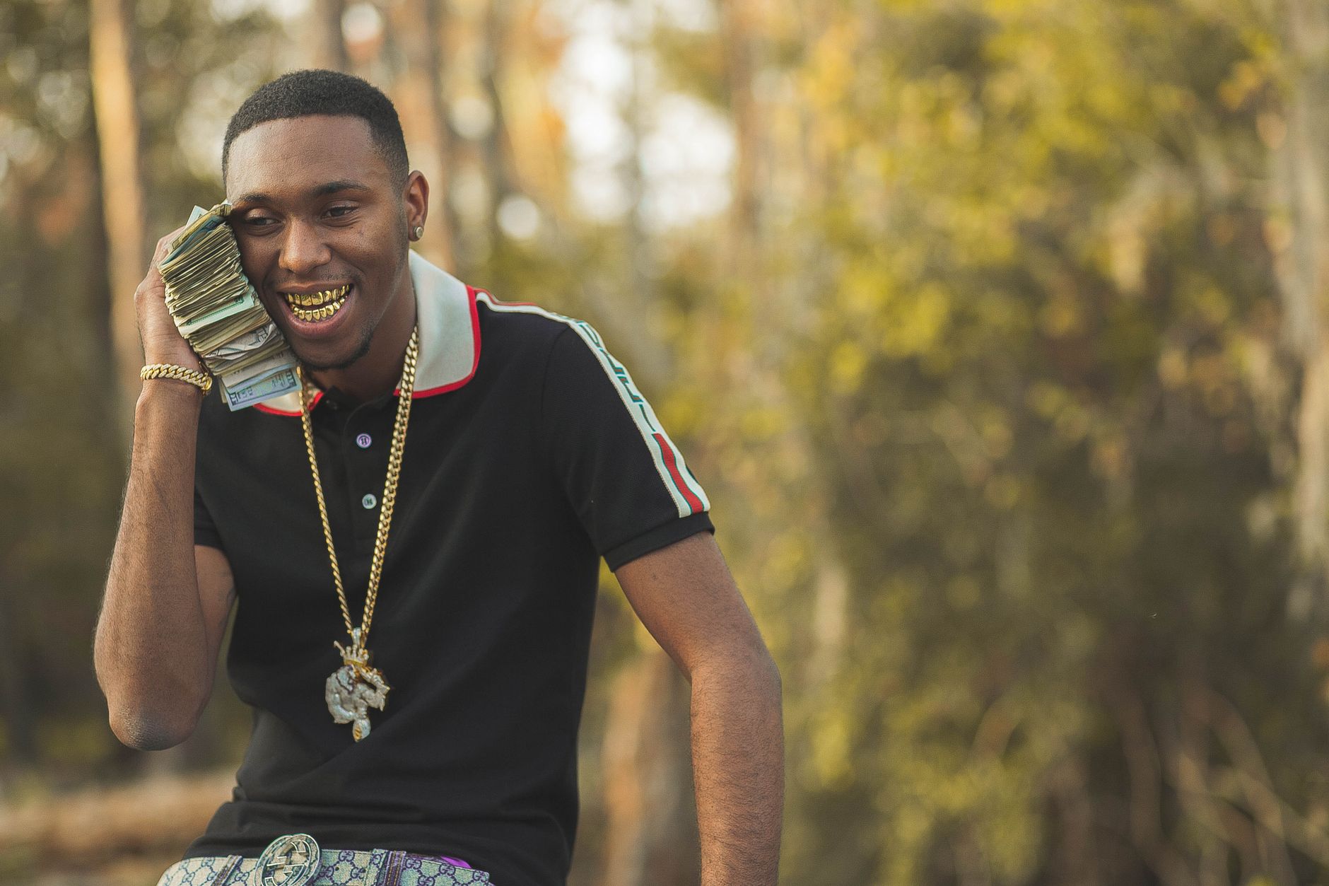 A man in a black shirt and gold chain talking on his phone