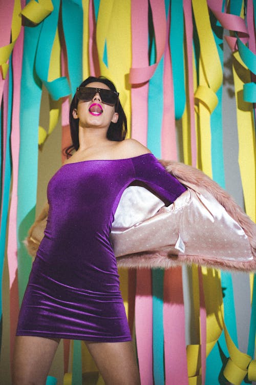 A woman in a purple dress posing in front of a wall of colorful ribbons