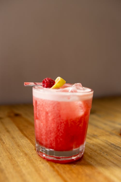A cocktail with a lemon wedge and raspberry garnish