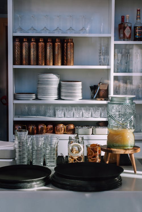 A kitchen with a counter and shelves filled with glassware
