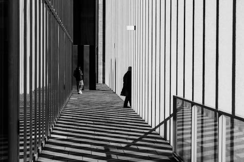 A black and white photo of a person walking down a walkway