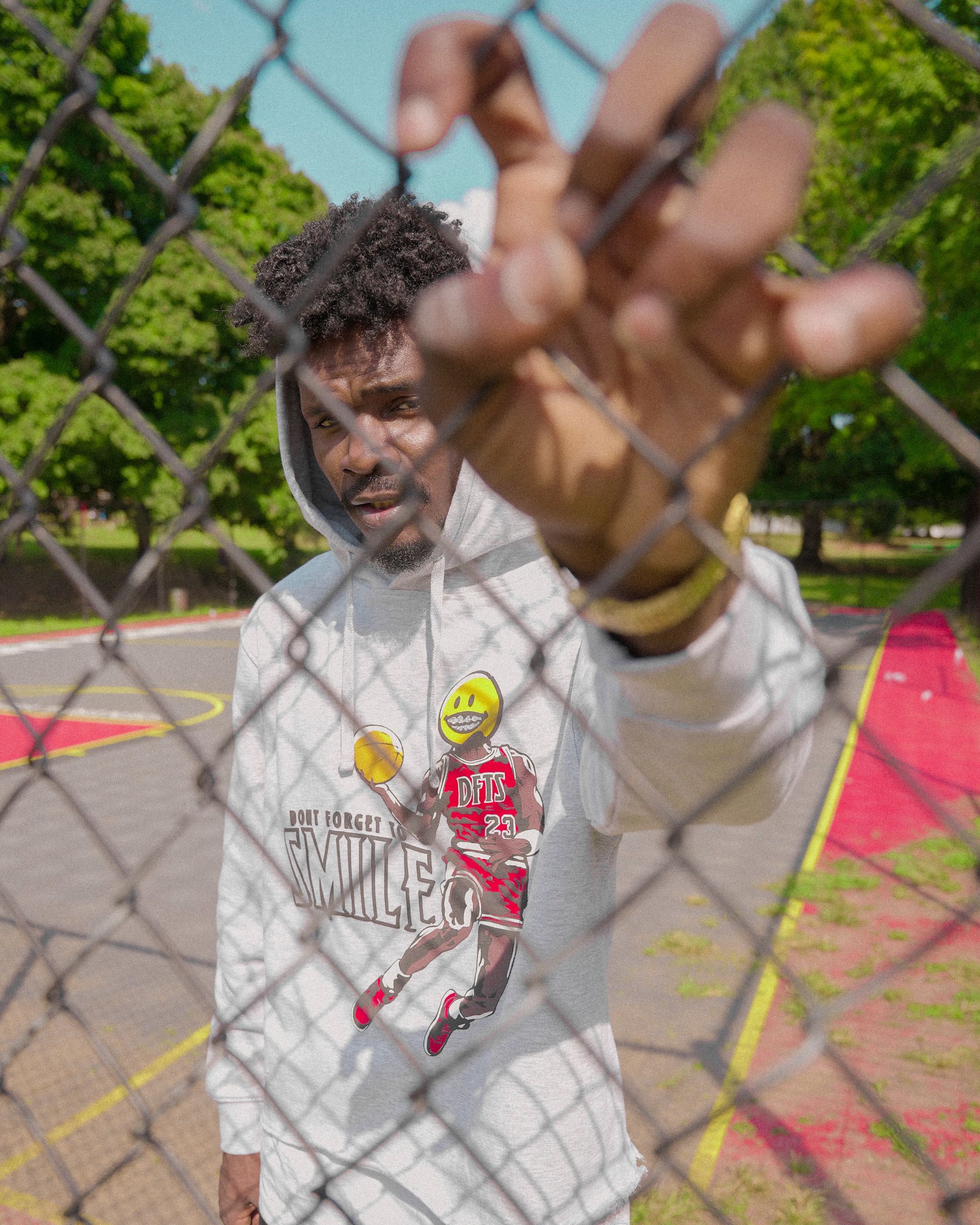 Fashion model poses through a fence on a sunny day at an Atlanta basketball court.