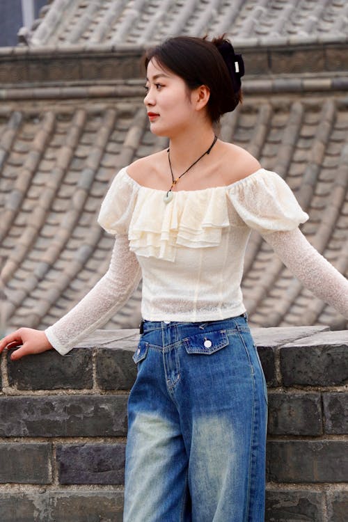 Woman Wearing a Blouse with Ruffles, and Blue Jeans, Posing against a Roof of a Chinese Building