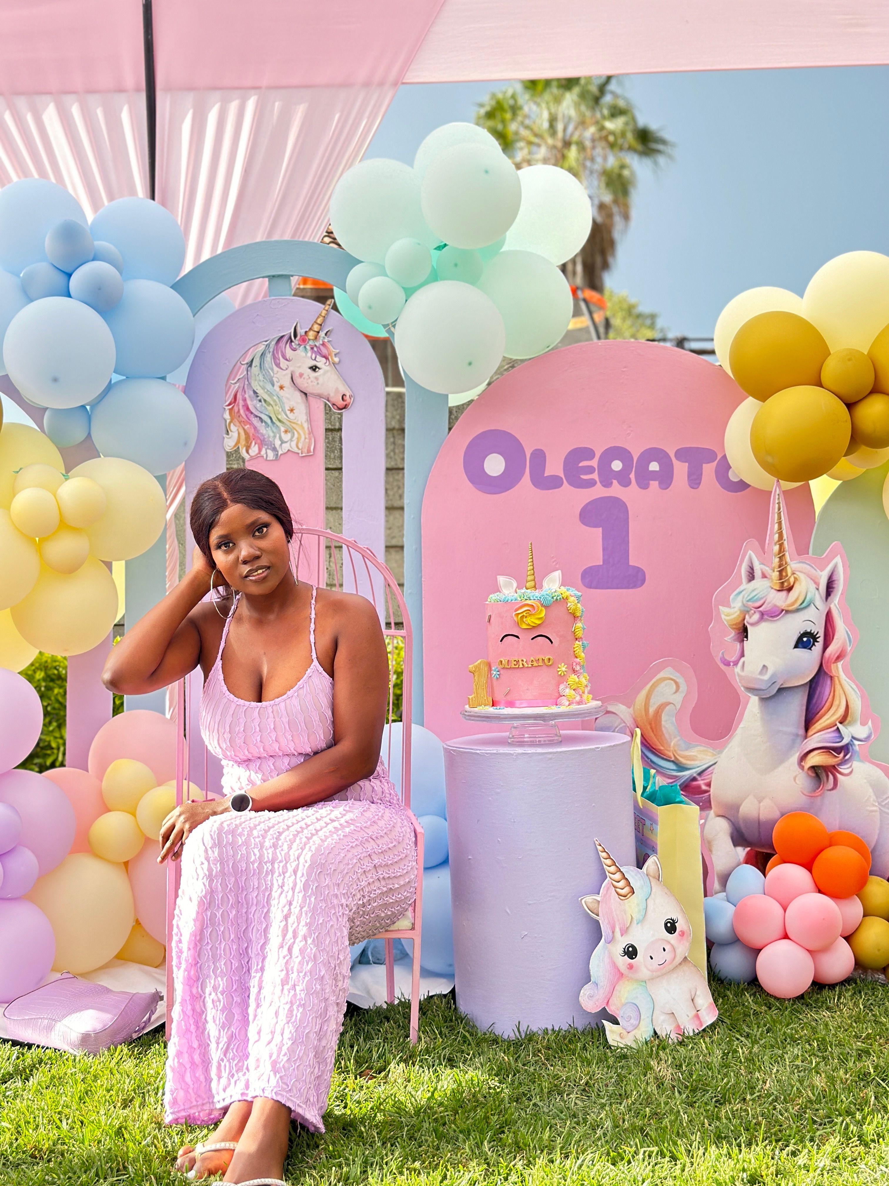 First birthday balloon decor ideas with woman sitting among pastel balloon decorations at a first birthday party