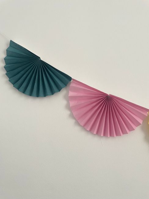 Vibrant green and pink paper fans hanging on a string for decorative purposes, ideal for parties.