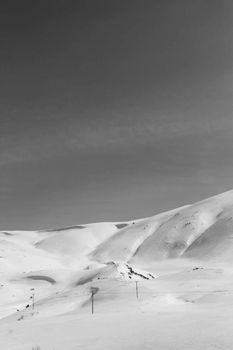 Black and white image of a tranquil snow-covered mountain slope under a clear sky.