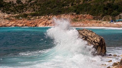 Free A large wave crashing into the shore near a rocky outcrop Stock Photo