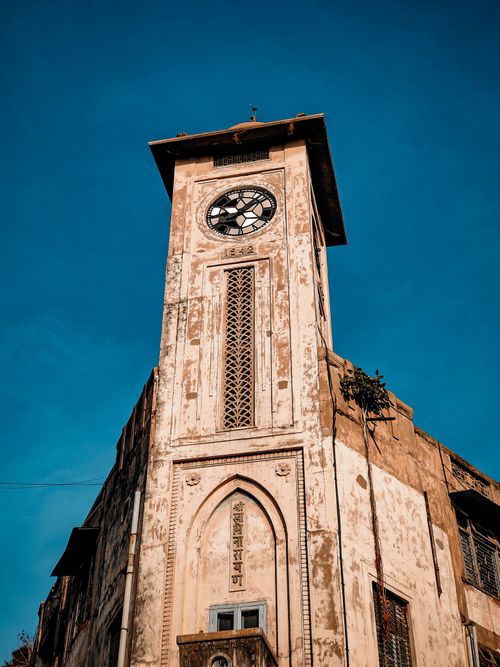Free Low-angle view of a historic clock tower in Ahmedabad, India, basking in sunlight against a vibrant blue sky. Stock Photo