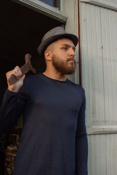 一名留着胡须的男子，穿着休闲服装，头戴帽子，手拿扳手摆出姿势，质朴而时尚