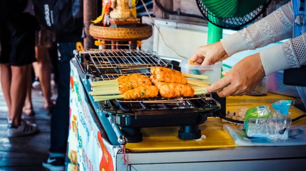 Street vendor grilling delicious satay skewers on an electric griller in an outdoor market.