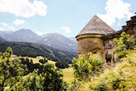 在郁郁葱葱的绿色和远处山脉映衬的明亮天空下，一座古老的石塔矗立在宁静的高山景观中