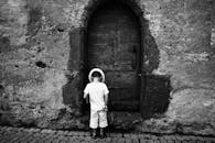 一张黑白照片里，一个戴帽子的孩子站在古老的石头门口