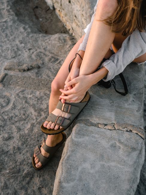 A woman in sandals sitting on rocks at Bondi Beach, Australia, during the day.
