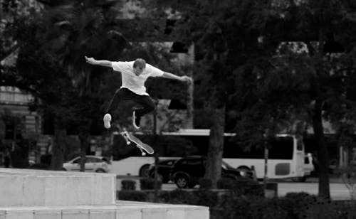 Man In Wit Overhemd En Zwarte Broek Skateboarden In De Buurt Van Groene Boom Overdag