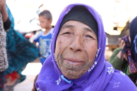 Close-up of an elderly woman wearing a purple headscarf and traditional facial tattoo in Bab Alhawa, Syria.