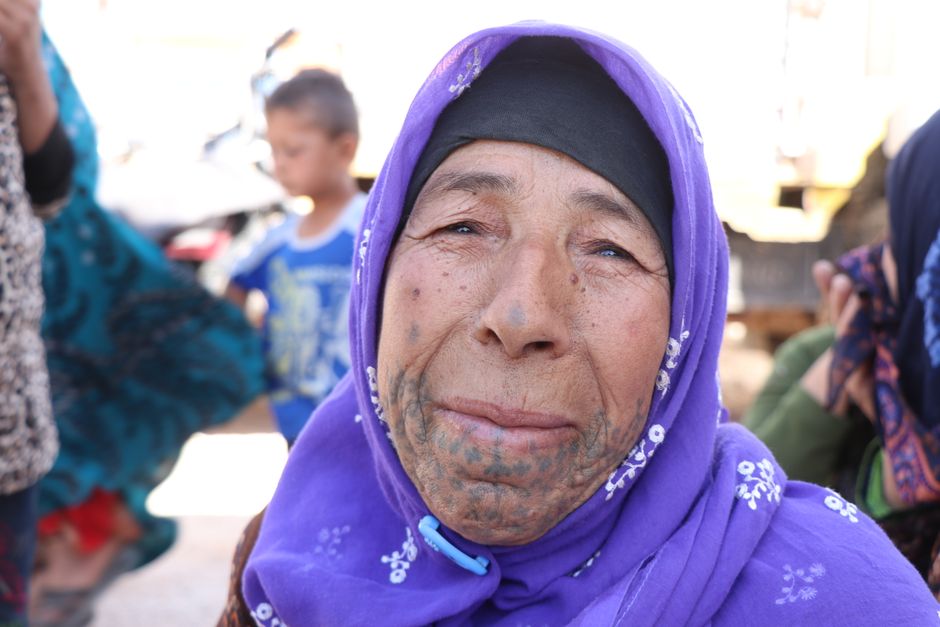 Close-up of an elderly woman wearing a purple headscarf and traditional facial tattoo in Bab Alhawa, Syria.