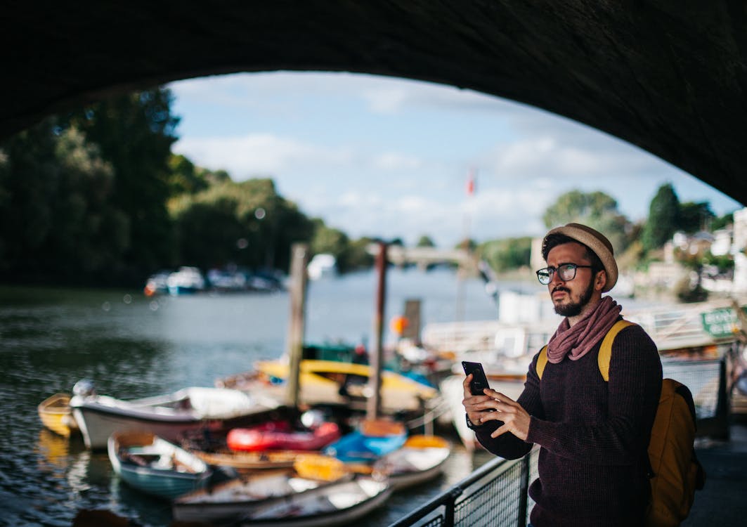 Hombre Sujetando Smartphone Cerca De Barcos