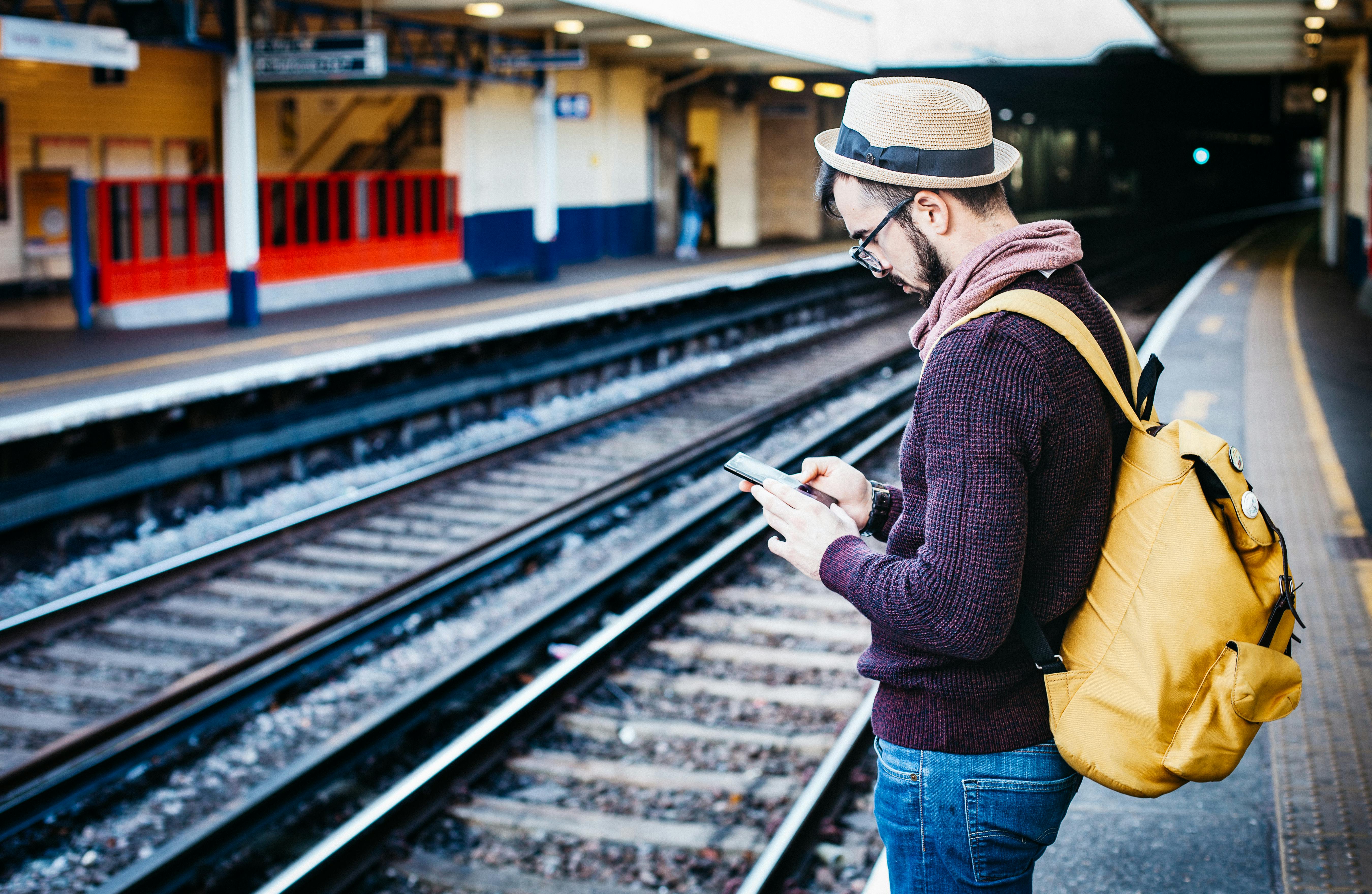 man in brown hoodie standing in front of train railway