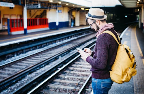 Мужчина в коричневой толстовке с капюшоном стоит перед поездом