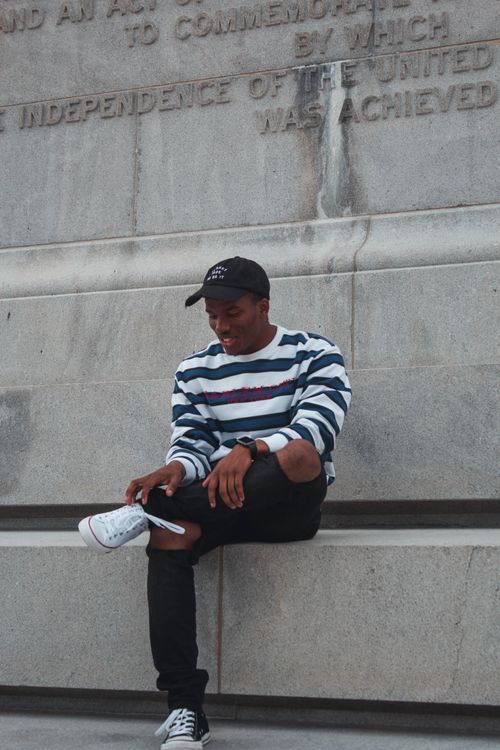 Free Young man in stylish attire sits on a historic monument, Williamsburg VA. Stock Photo
