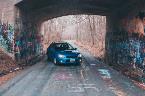 Free Blue car parked under a graffiti-covered overpass in Williamsburg, Virginia on a cool day. Stock Photo