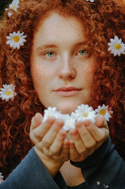 Portrait of a woman with red curly hair and daisies, showcasing natural beauty and style.