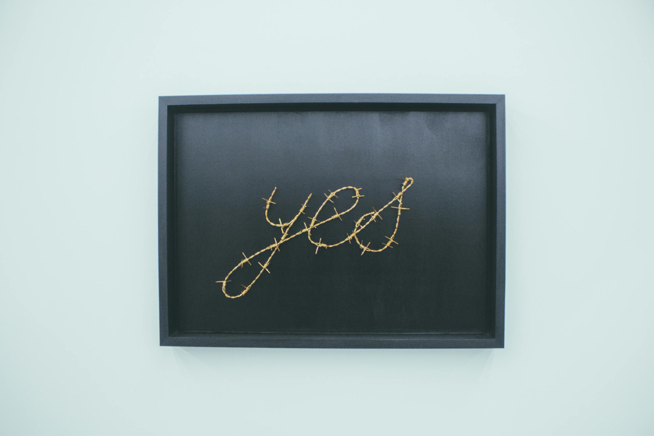 Image of the word yes on a black picture hanging on a green wall. 