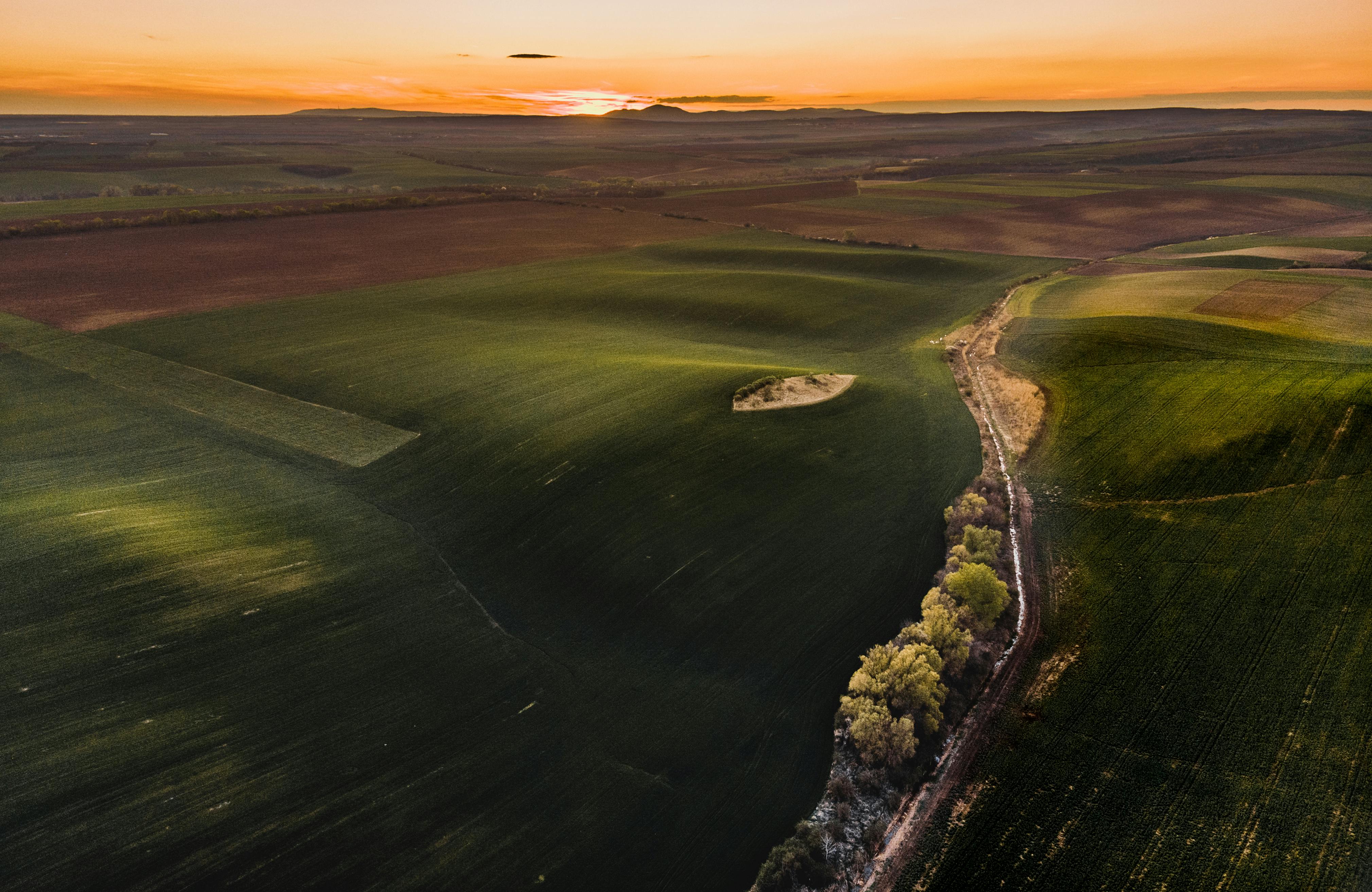 日落时分，广阔的绿色田野映衬着橙色的天空，构成了一幅展现大自然宁静之美的空中景观