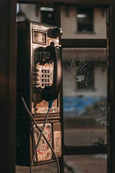 A vintage telephone booth with a rusty exterior on an urban street.