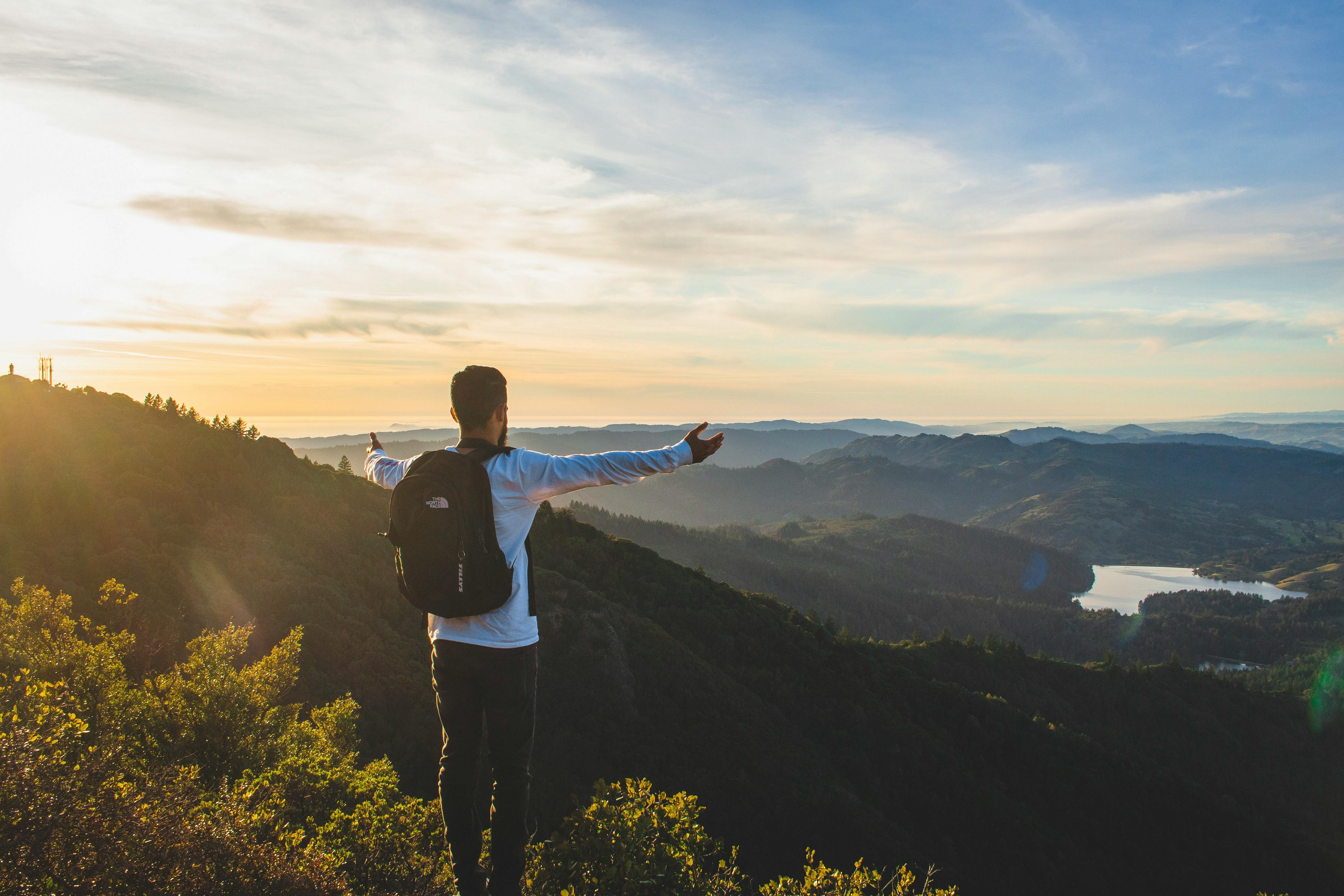 日出时分，一名背着背包的男子欣赏着周围环绕着大自然的广阔山景