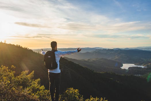日出时分，一名背着背包的男子欣赏着周围环绕着大自然的广阔山景