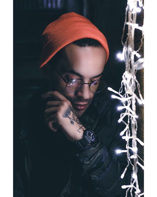Portrait of a man with an orange beanie and string lights, exuding a stylish and moody vibe.