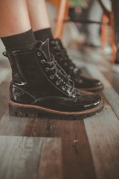 Fashionable black leather boots with laces on a wooden floor indoors.