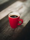 一张质朴的木桌上，放着一杯装在充满活力的红色马克杯里的温暖黑咖啡