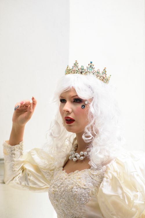 Free Portrait of a woman in a white dress and wig, wearing a jewel-encrusted crown. Stock Photo